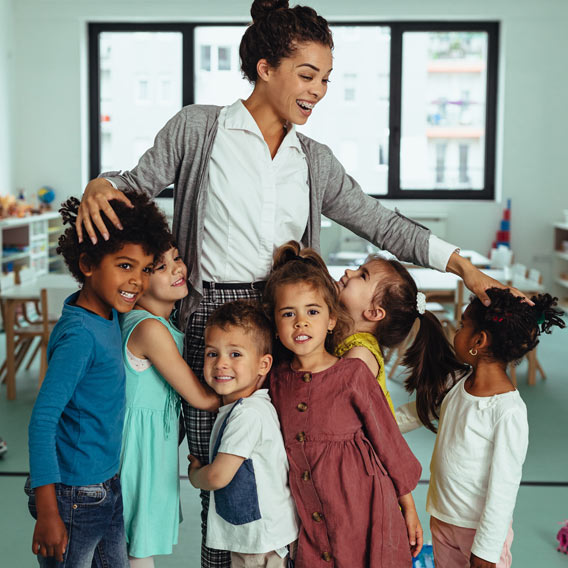 Photo of a happy female teacher surrounded by her students giving her hugs
