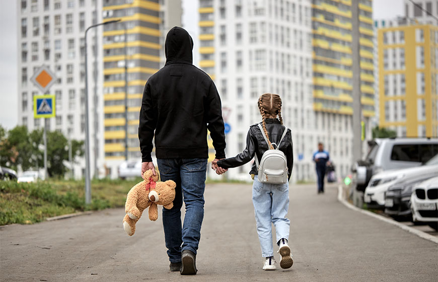 Photo of a little girl walking with a man holding her stuffed teddy bear
