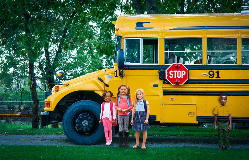 Photo of children standing beside a school bus